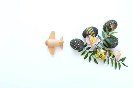 Wooden toy airplane lucky black easter eggs with gold decor and pink flowers. Happy Easter concept.