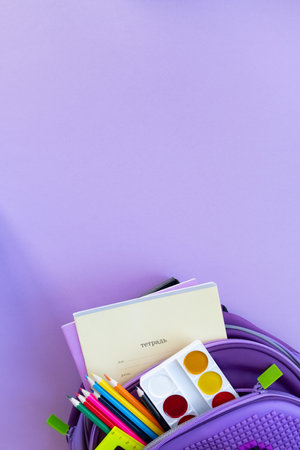 Back to school concept. Backpack with school supplies on purpple background. Top view. Copy spaceの写真素材
