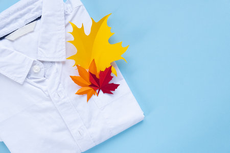 A white shirt with autumn leaves in the pocket. Back to school concept. The leaves are cut out of paper. Shirt on a blue backgroundの写真素材