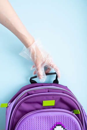Back to school concept. The concept of virus infection, quarantine in schools, a gloved hand holding a school satchelの写真素材