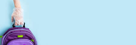 Back to school concept. The concept of virus infection, quarantine in schools, a gloved hand holding a school satchelの写真素材