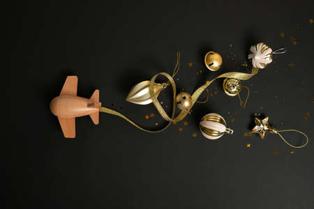 wooden children's plane with different christmas gold decoration on a black background. Merry christmas concept. Airplane lucky new year. Holiday comes to usの写真素材