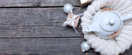 White teapot with hot tea, white knitted woolen scarf with white Christmas balls and gifts. Holiday conceptの写真素材
