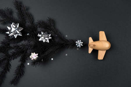 Happy New Year and Merry Christmas black concept. Wooden children's plane with different christmas decoration on a black background. Airplane lucky new year. Holiday comes to us.の写真素材