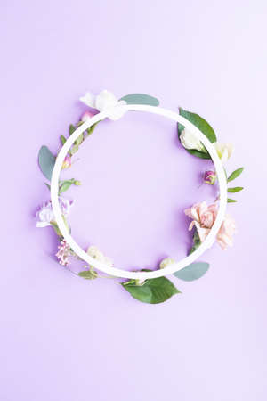 Round frame wreath with pink roses, white flowers, branches, leaves and petals on purple background. Flat lay, top viewの写真素材