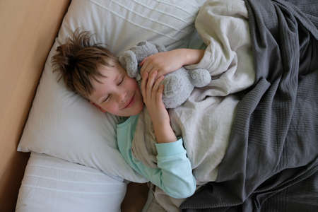 The child is lying with a fever in bed with a plush toy