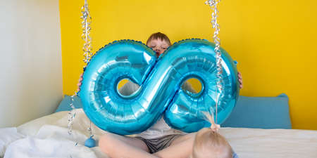 A boy holds a balloon in the shape of the number 8, he communicates with his younger sister