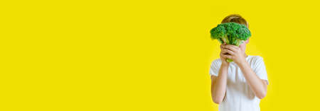 A boy 7 year old with broccoli on yellow background. The concept of healthy food, vitamins from...
