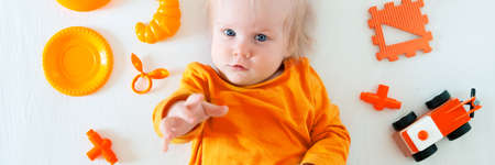 A little Caucasian girl is playing with toys on a white background. 1 year old, the child is wearing an orange T-shirt and playing with orange toysの写真素材