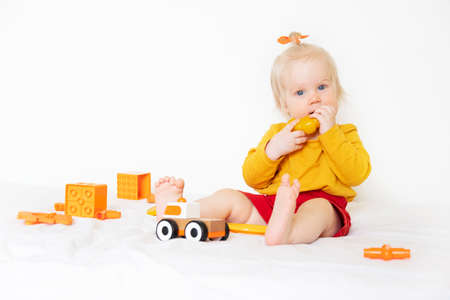 A little Caucasian girl is playing with toys on a white background. 1 year old, the child is wearing an orange T-shirt and playing with orange toysの写真素材