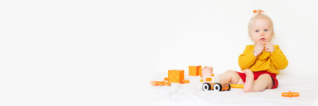 A little Caucasian girl is playing with toys on a white background. 1 year old, the child is wearing an orange T-shirt and playing with orange toysの写真素材