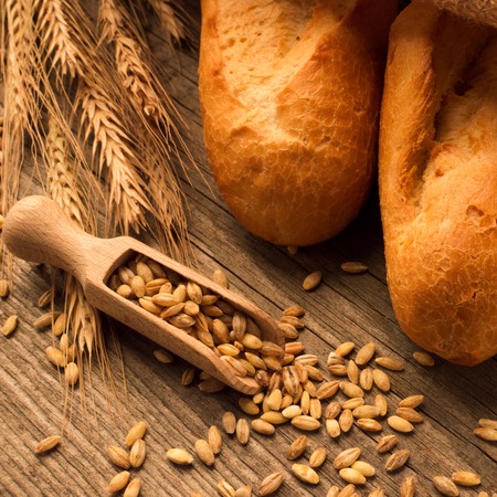 Spoon with grain, bread, baguette, loaf and buns on the wooden desk