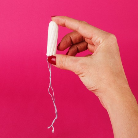 Woman holding menstrual tampon on a pink background. Menstruation time. Hygiene and protection.の写真素材