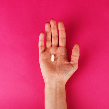 Woman's hand holding a pill on the pink background.