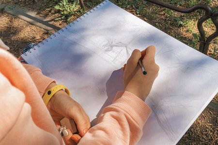 Girl drawing with black pencil a fantasy sketch in sketchbook.  Plein Air in the park.の写真素材