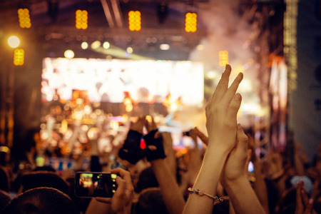 Audience with hands raised at a music festival and lights streaming down from above the stage.の写真素材