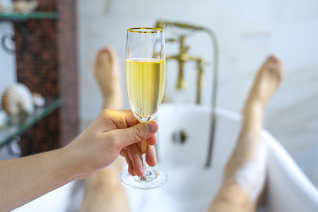 Close-up of a glass of champagne against the background of a relaxed male bathing in a bubble bathの写真素材
