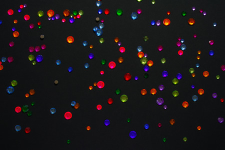 Top view on the multi-colored colorful rhinestones scattered on a black background. Abstraction.