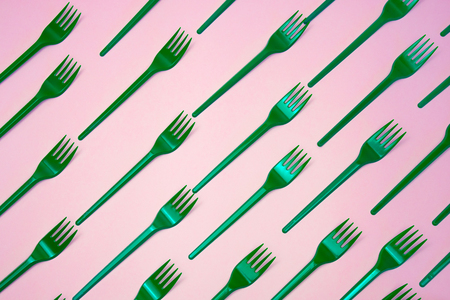 Many green plasic forks  on pink background, top view.の写真素材