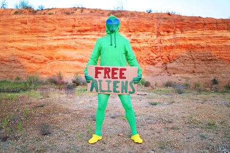 a man dressed in a green alien carnival costume suit at a lone rally with a sign free aliens on the...