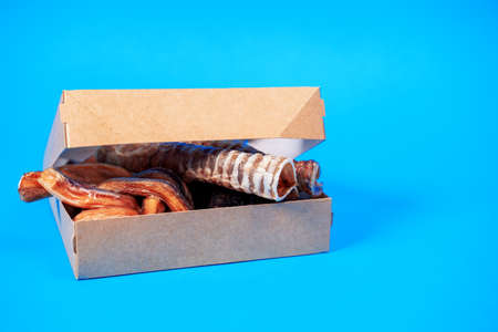 craft open box with many many diverse tasty dried snacks for pets inside on blue background, close up, top view, copy space for advertising text. Pet care. Pet supplies.の写真素材