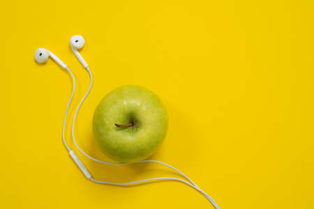 Green apple and white wired headphones on a bright yellow background.の写真素材