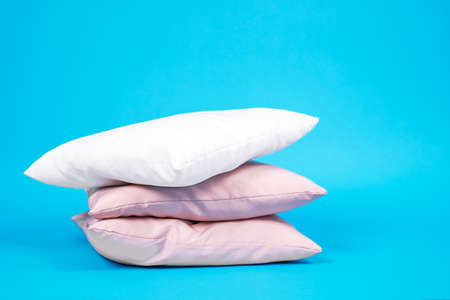 Three pillows stacked on top of each other, white and pink color, on bright blue background. Bed linen and bedding, housekeeping. Indoors, copy space.の写真素材