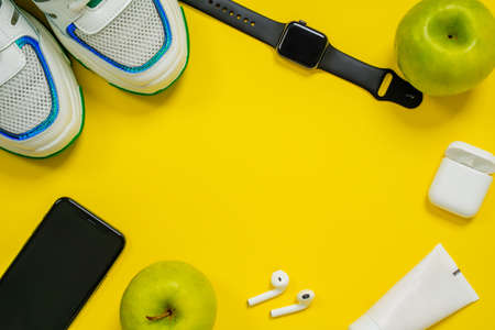 Set of modern active person with healthy athletic lifestyle. Mobile phone, wireless headphones, smart watch, stylish sneakers, cream tube and green apples on yellow background, top view, copy spaceの写真素材