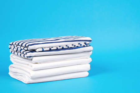 Striped and snowy white bed linen, neatly folded sheets on blue background. The concept of cleanness and proper storage organization. Indoors, copy space.の写真素材