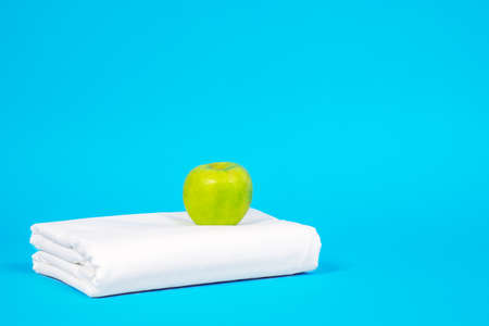 Fresh green apple above snowy white bed linen, neatly folded sheet on blue background. The concept of cleanness, freshness and domestic or hotel storage organization. Copy space.の写真素材