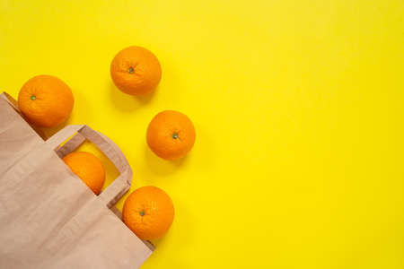 Some oranges rolling out from the cardboard package on bright yellow surface. Craft organic pack and natural product, ecological healthy concept. Indoors, copy space.の写真素材