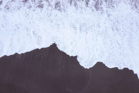 Top view from the drone on the stormy sea, white foam of waves and the beach.