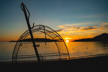 traditional small net for catching crabs or fish against a beautiful sunset on the seaの写真素材