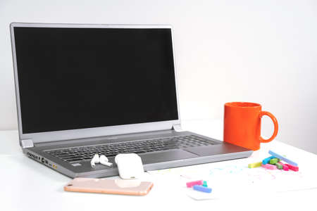 The wireless laptop, standing on a white table, on light background. Next to a bright orange cup,...