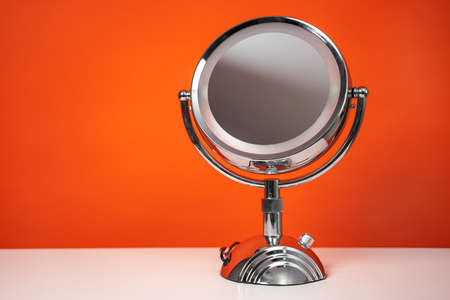 Chromed steel round magnifying mirror on handle set up on the white table. Bright orange background, single object, copy space.の写真素材