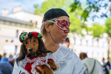 Russia, St. Petersburg, May 25, 2019: Portrait of a red dachshund dog sitting on his owner's hand, dressed in a cordinal costume, in the park at a parade festival dachshund in St. Petersburgのeditorial素材