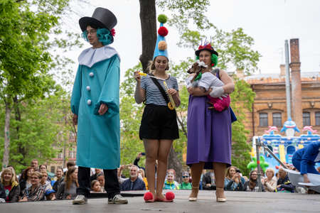 Russia, St. Petersburg, May 25, 2019: Event with dogs called Dachshund Parade. Costume procession, three people and pretty dog in vibrant clown costumes on the stage with viewers around there.のeditorial素材