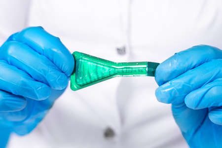 Doctor in medical coat and sterile protective silicone gloves open bottle of medication according to...