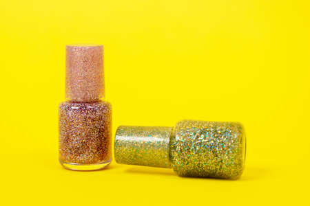 Bottles of shiny nail polishes with shimmering effect on yellow background, front view, copy space for advertising. Glitter skin decoration for party.の写真素材