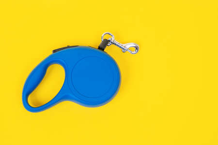 Blue plastic durable and ergonomic leash roulette for pets on yellow background, top view, copy space. Convenient mechanical device for keeping and controlling dog in streetの写真素材