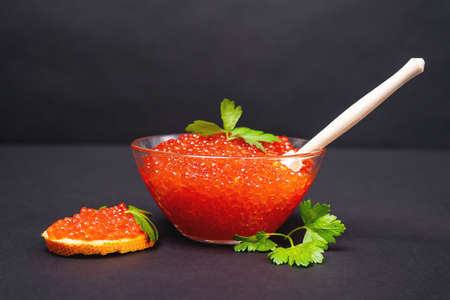 National Russian holiday delicacy - red salmon caviar in glass bowl with wooden spoon and on piece...
