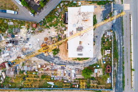 Aerial view from the copter on unfinished builidng among the city, industrial equipment, crane,...