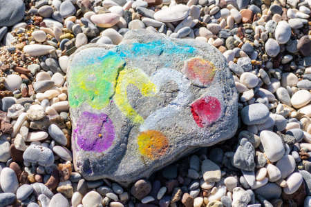 Heart with rainbow circles is painted on stone lying on pebbles beach. Meditation, therapy, development, calmness and rest.の写真素材