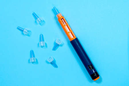 Insulin syringe pen with specialized needles scattered around to give injection to person with diabetes. blue background, top view, copy space. Equipment for providing specialized first aid.の写真素材