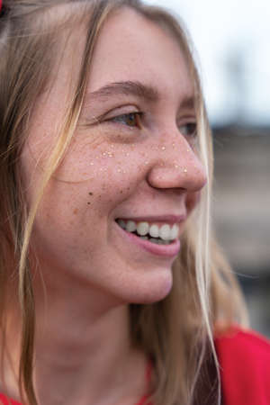 Vertical portrait of young smiling blonde woman with a soulful and playful look, freckles on her...