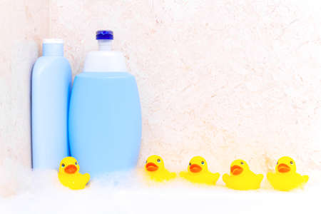 On the side of the tub there are yellow rubber ducks for bathing covering with foam and plastic bottles of shower cosmetics, empty templates for advertising labels on bottles.の写真素材