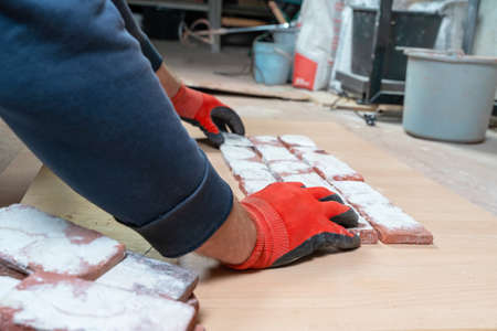 Artisan puts together plaster casts of bricks covered with whitewash to make tiles for interior decoration or facades of buildings, side view. Workflow in the design workshopの写真素材