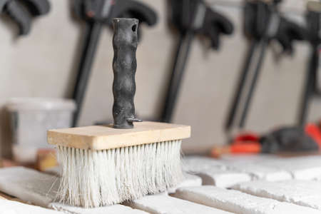 Large brush, which artisan used to clean surface of decorative tiles from dust, stands on desk in foreground, close up, side view. Other working tools and gloves in blurred backgroundの写真素材