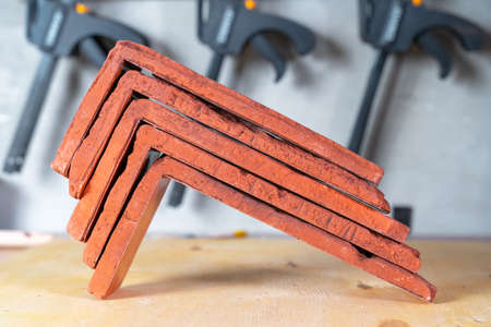 Stack of red finishing plaster corners for decorative tiles imitating brickwork lying on the desk in...