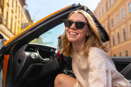 Portrait of attractive blonde young woman in sunglasses, who is looking out of a convertible car,...